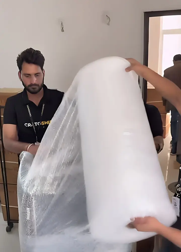 Uniformed CratoShift packer rolling bubble wrap around a wrapped armchair