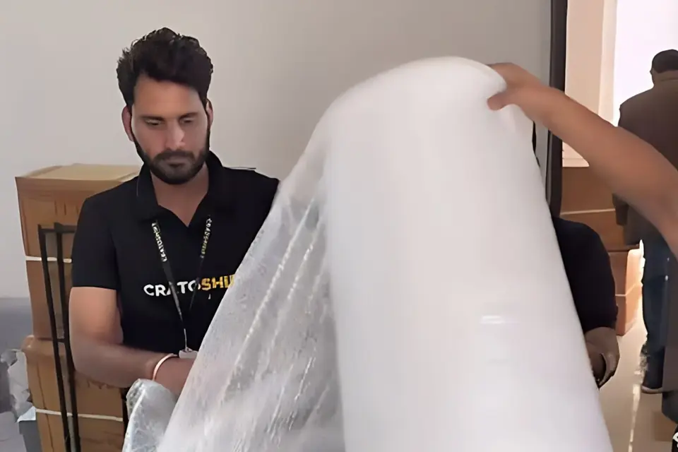 A CratoShift packer rolling bubble wrap over a stretch-wrapped armchair during a house move